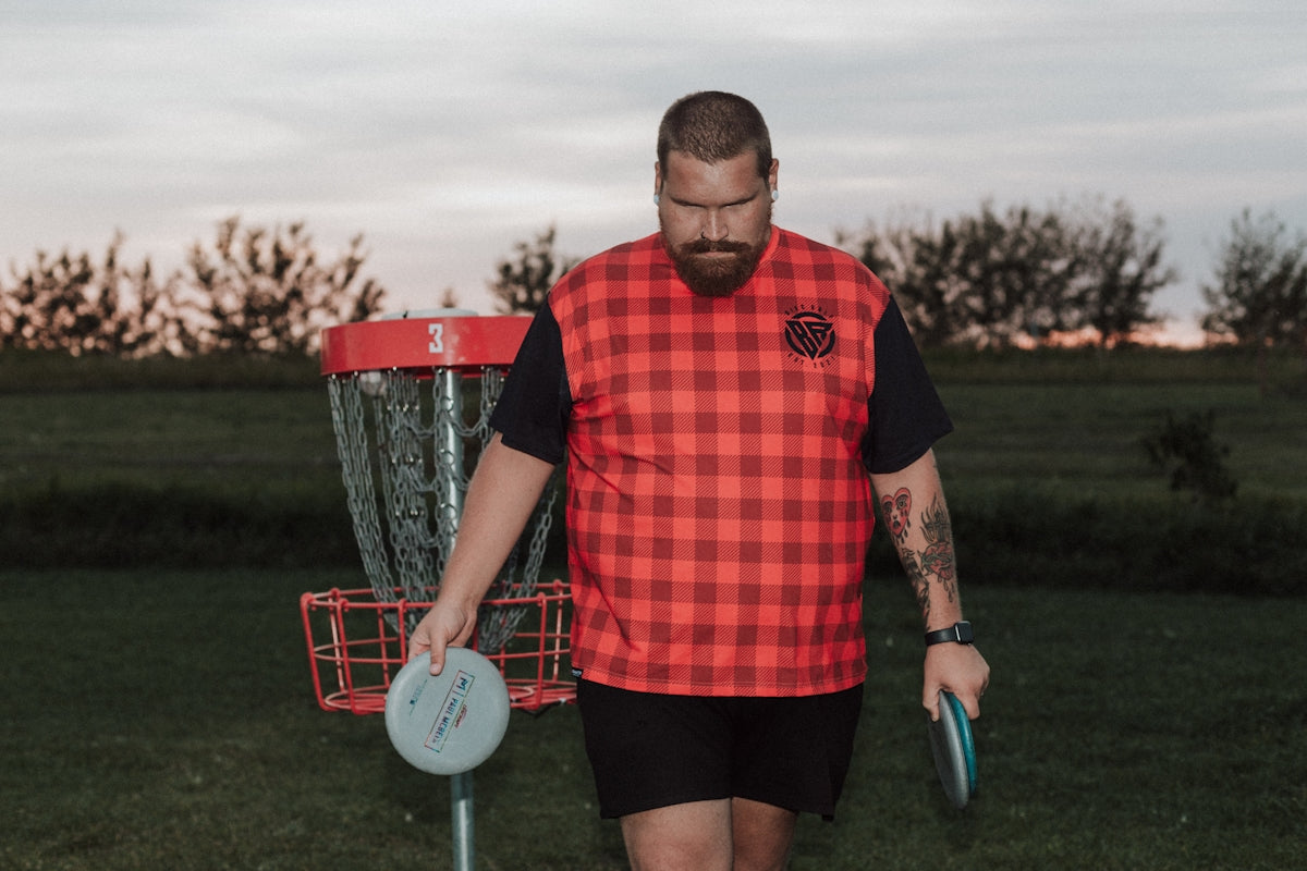 A man holding a frisbee standing next to a frisbee golf net